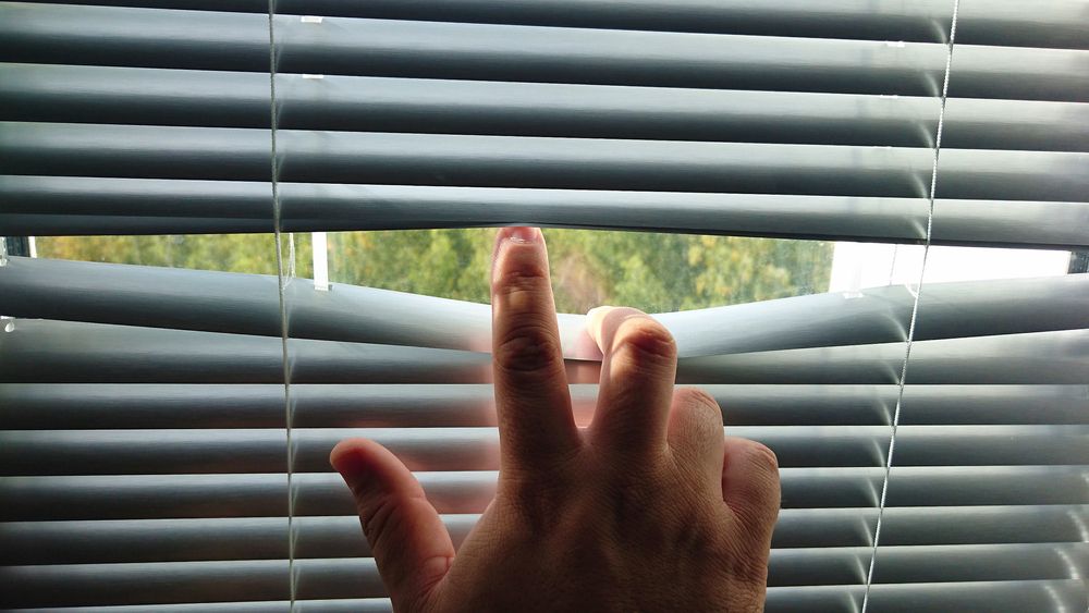 Man's hand revealing white venetian blinds.Hand Opening slats of Venetian blinds with a finger